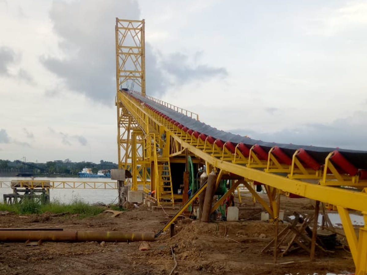 Konveyor rangka kuning menuju dermaga, dilengkapi idler pengangkut material curah