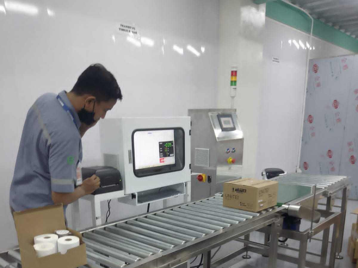 Check weigher terpasang pada jalur konveyor rol, dioperasikan seorang teknisi di ruang produksi