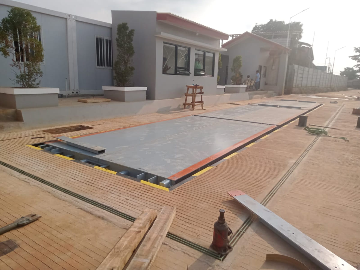 Deck jembatan timbang sedang dipasang di atas pondasi beton di area pabrik