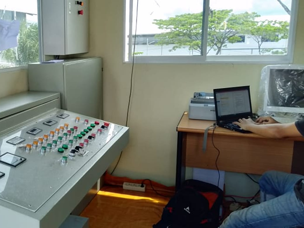 Meja panel kontrol dengan deretan tombol operator dan laptop commissioning di ruang kendali