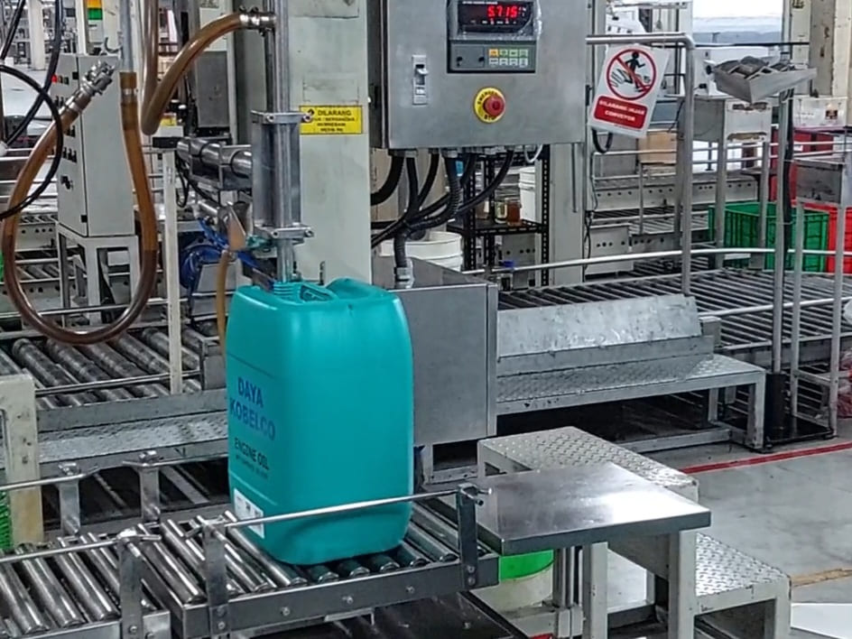 Filling machine mengisi jeriken di atas konveyor rol, dipandu panel kontrol dan indikator bobot